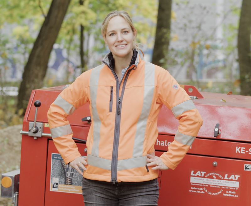 Larissa Zeichardt, Geschäftsführerin von LAT, steht in orangener BP® Warnschutzjacke vor einer Baumaschine.